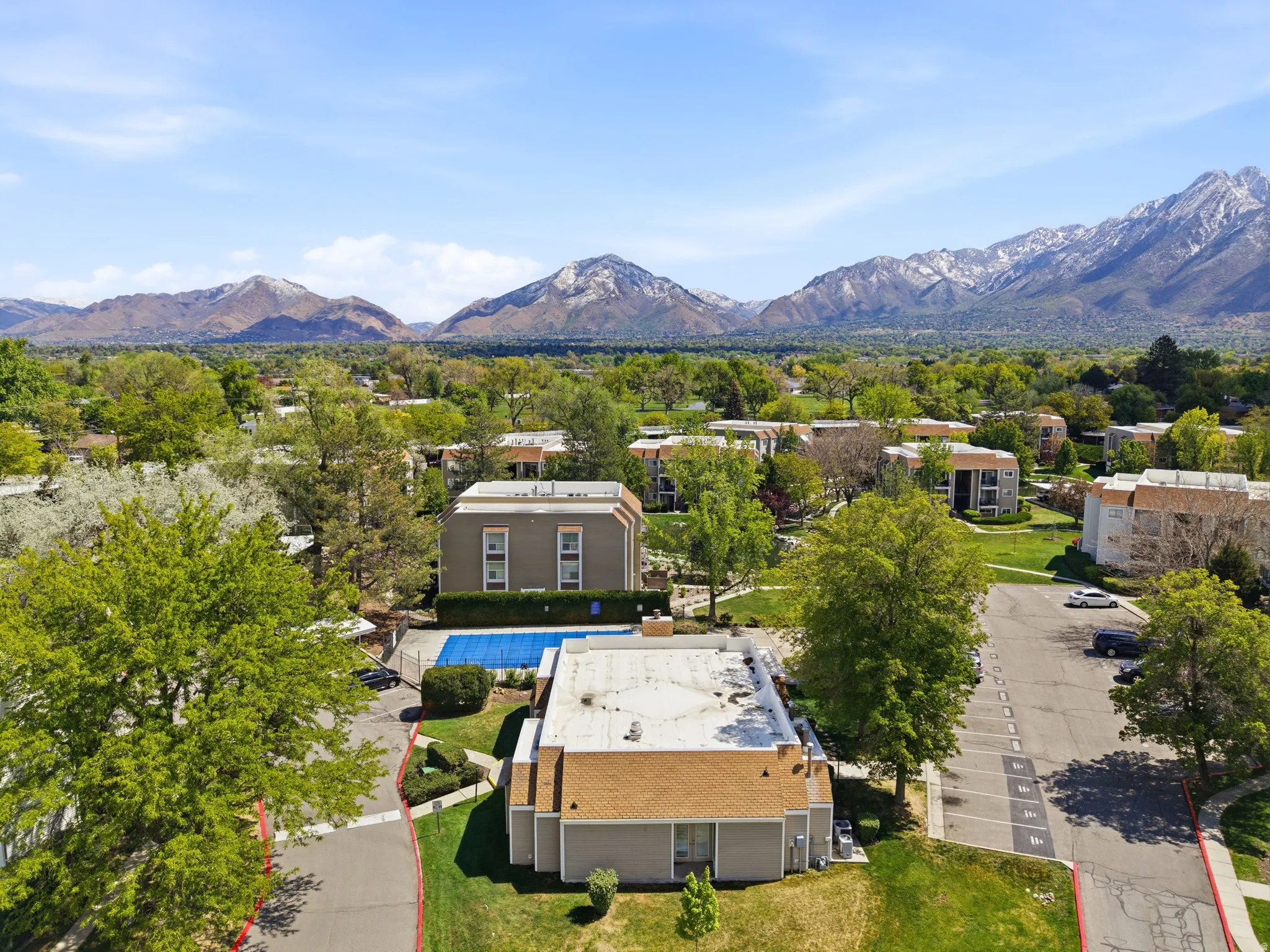 Aerial perspective showcasing multiple residential buildings, verdant landscaping, parking areas, and an outdoor swimming pool