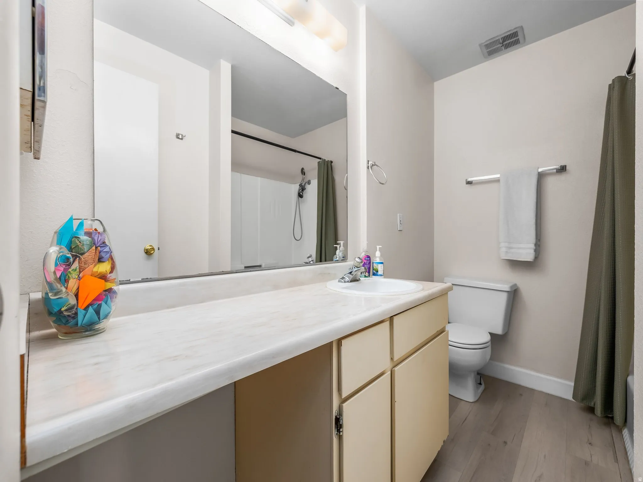 Bathroom featuring a single vanity with an integrated sink, cream-colored cabinetry, a large wall-mounted mirror, and wood-finish flooring