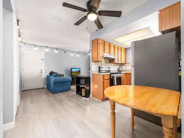 Open-concept living area featuring light wood-finish flooring, a kitchen with wood cabinetry and a tile backsplash, and a dining area with a light wood table