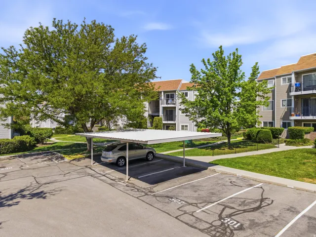 Designated carport parking space with a protective metal roof, surrounded by mature trees and manicured green spaces