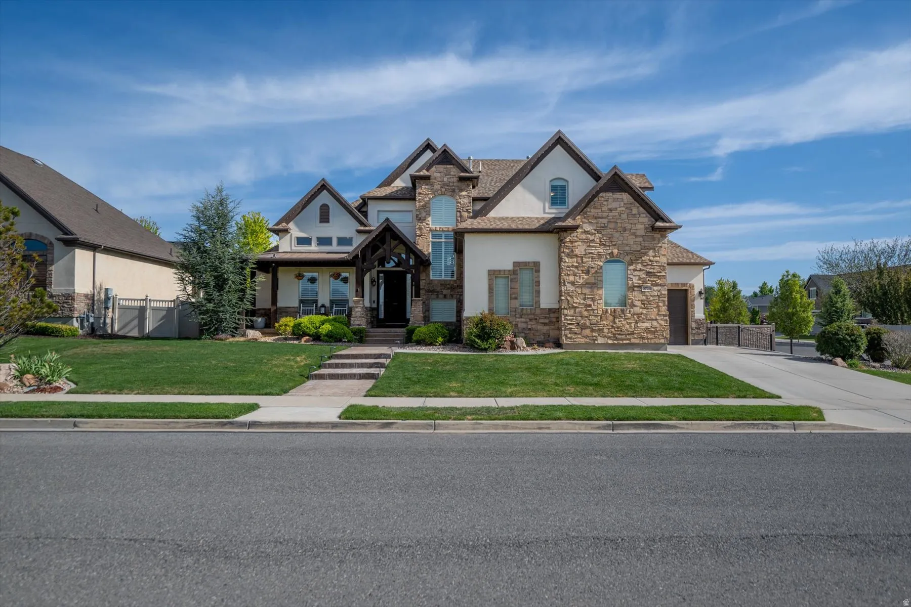 Stately exterior featuring stone and stucco accents, a covered front porch, a multi-car driveway, a meticulously maintained lawn, and mature landscaping