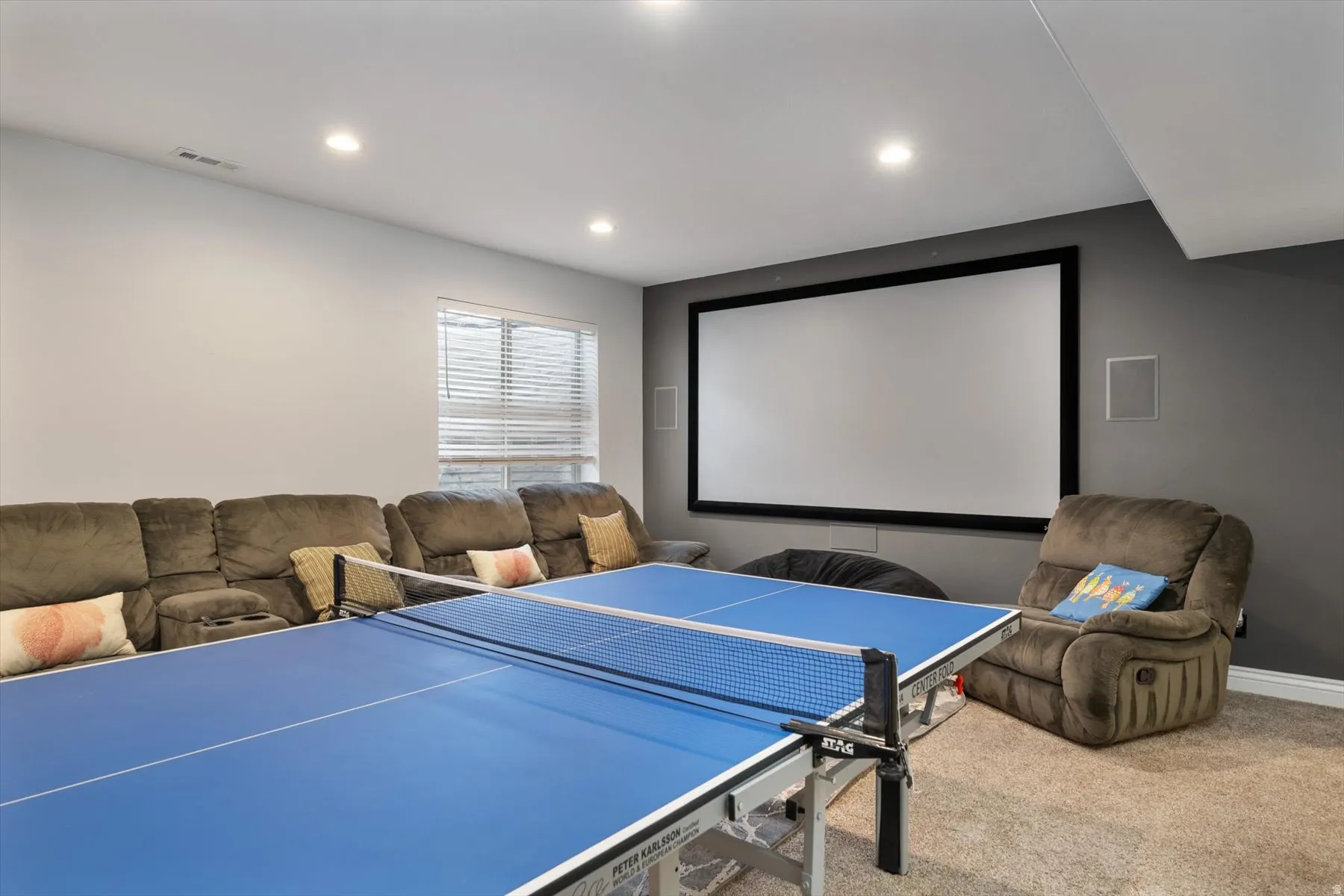 Recreational space featuring a large projection screen, recessed lighting, and a window with blinds