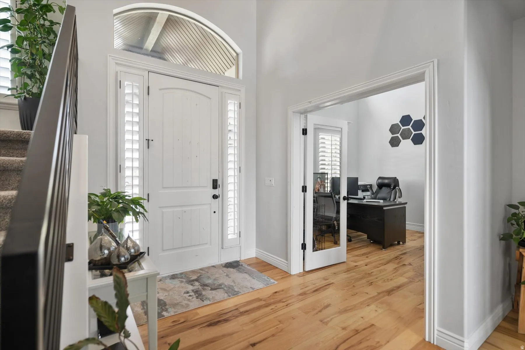 Grand entry featuring a white arched door with transom window and sidelights, wood-finish flooring, and a carpeted staircase with dark railings