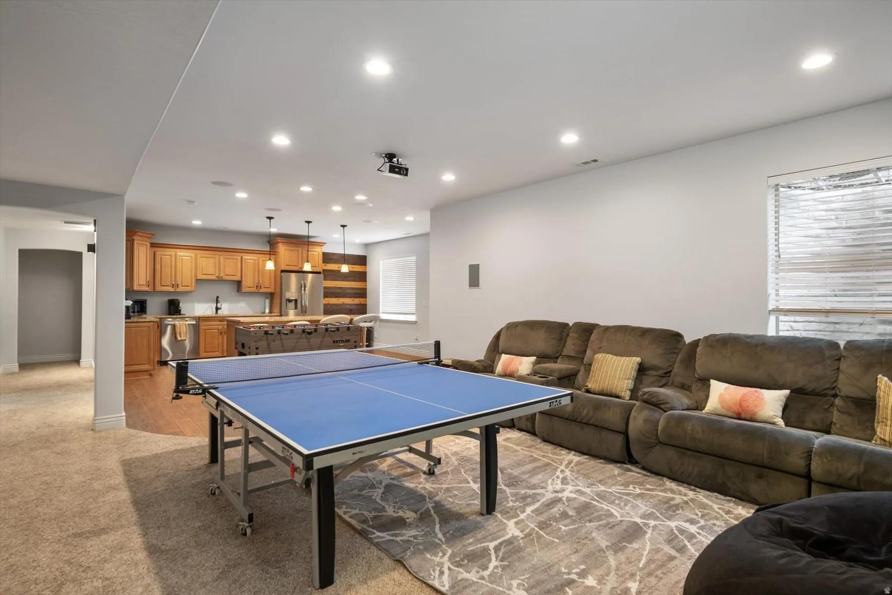Spacious recreation room featuring recessed lighting, a built-in wet bar with wood cabinetry and stainless steel appliances, and a window with blinds