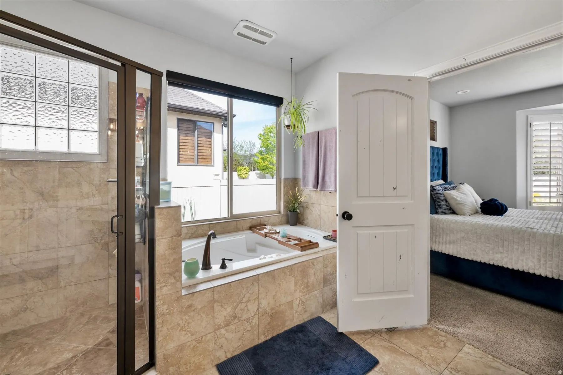 Primary bathroom ensuite with soaking jetted tub with bronze faucet, glass-enclosed shower with bronze frame, large window, & tile flooring