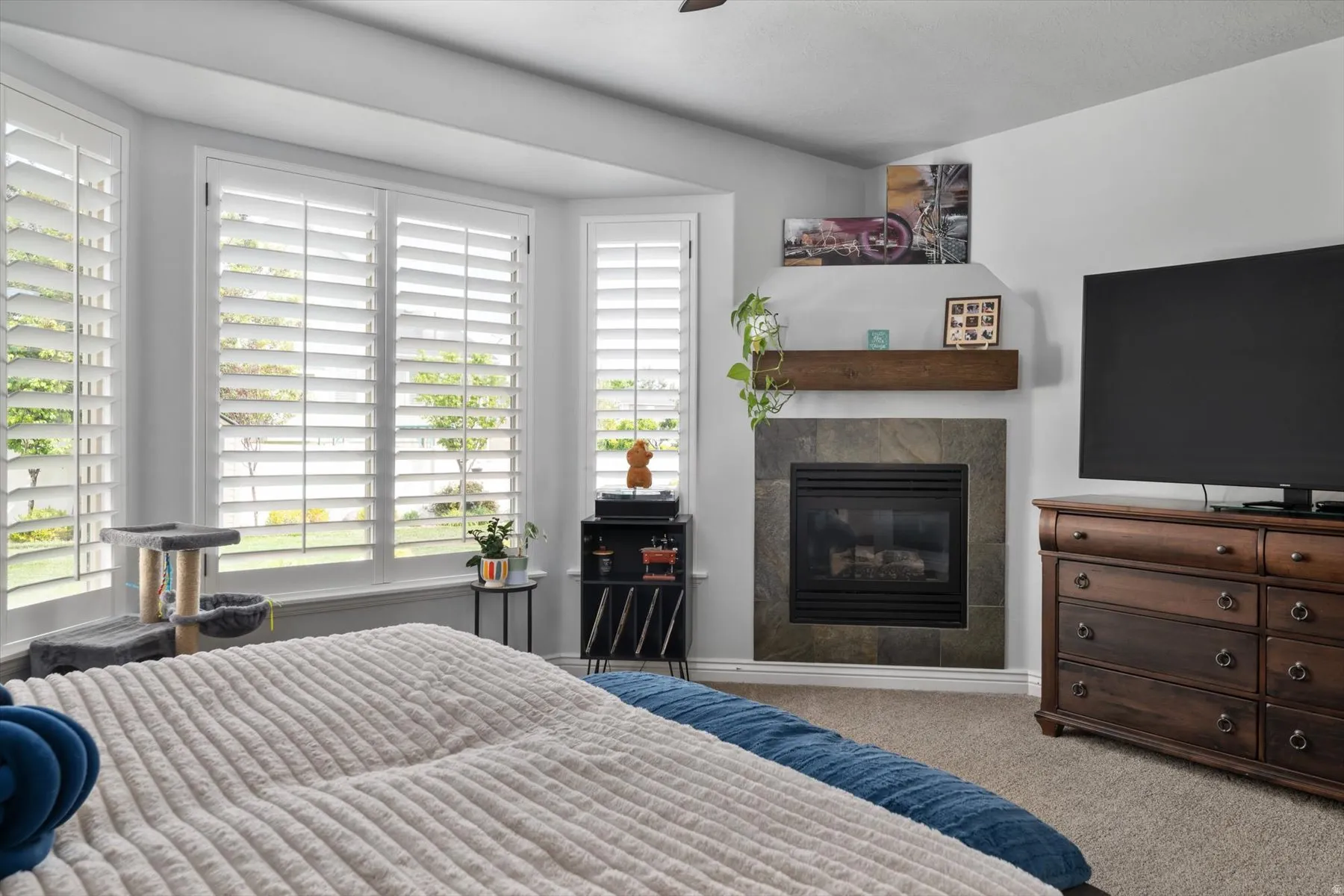 Primary bedroom with bay window with white plantation shutters gas fireplace