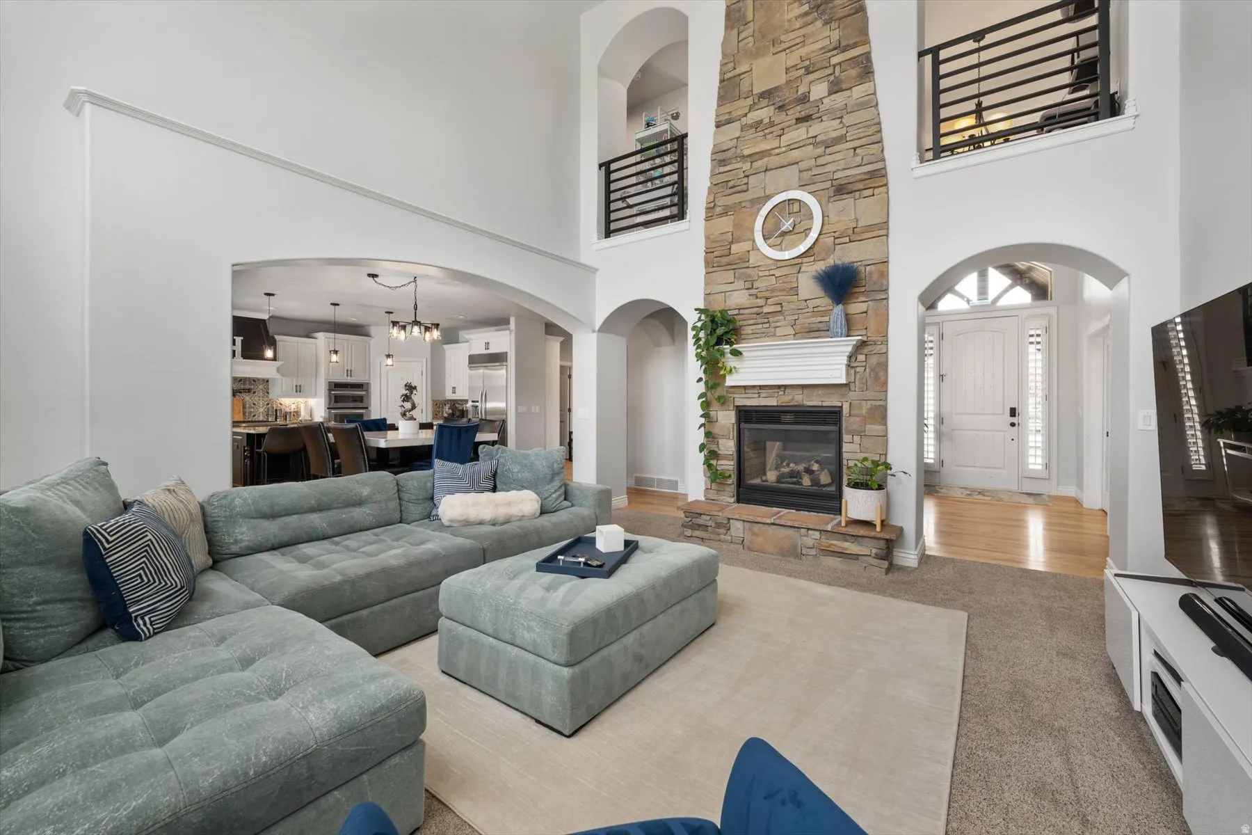 Two-story living area featuring a stacked stone fireplace with a white mantel, arched doorways, and light wood-finish flooring in the entryway