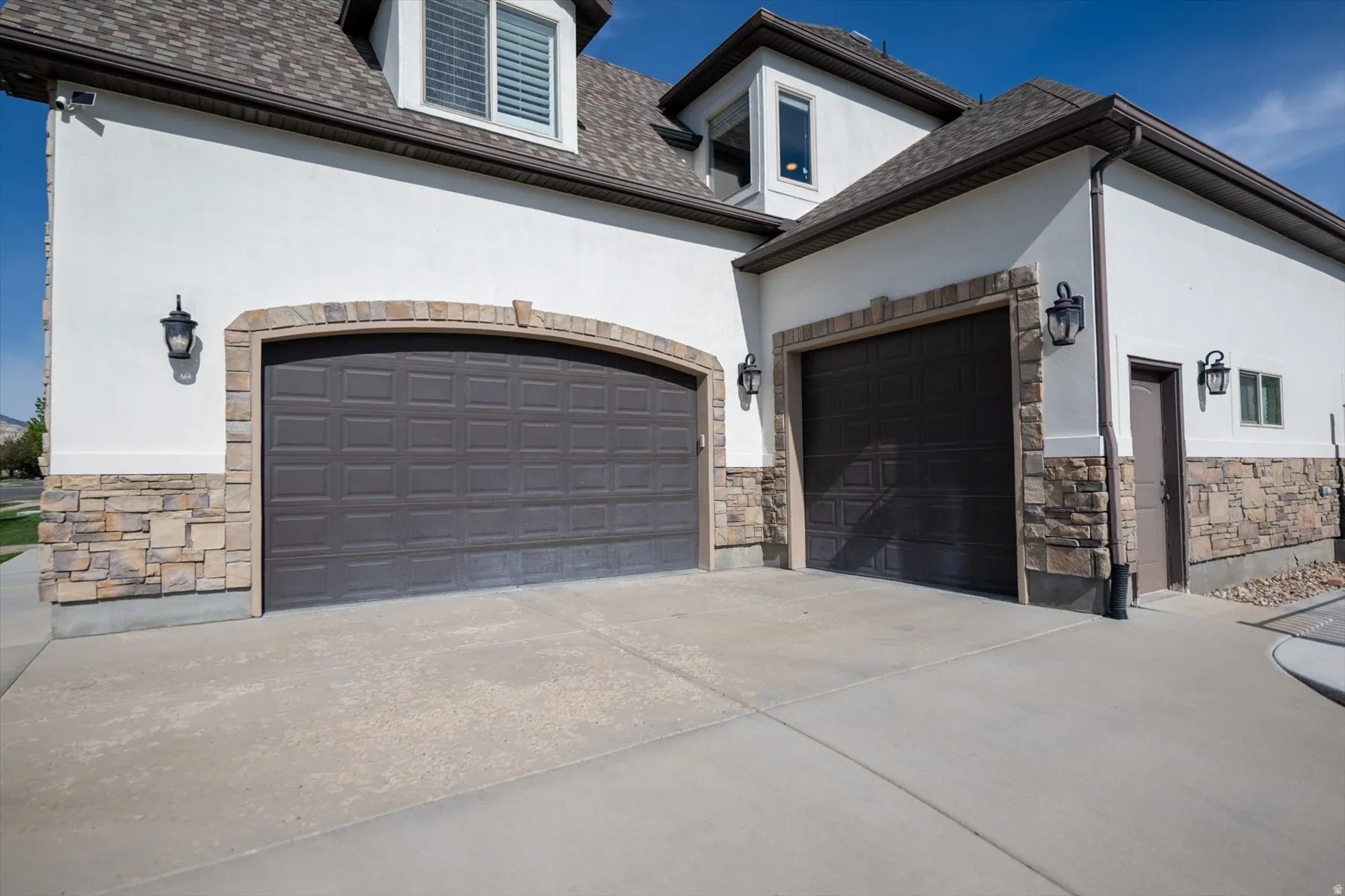 Exterior featuring two dark brown paneled garage doors with arched stone surrounds