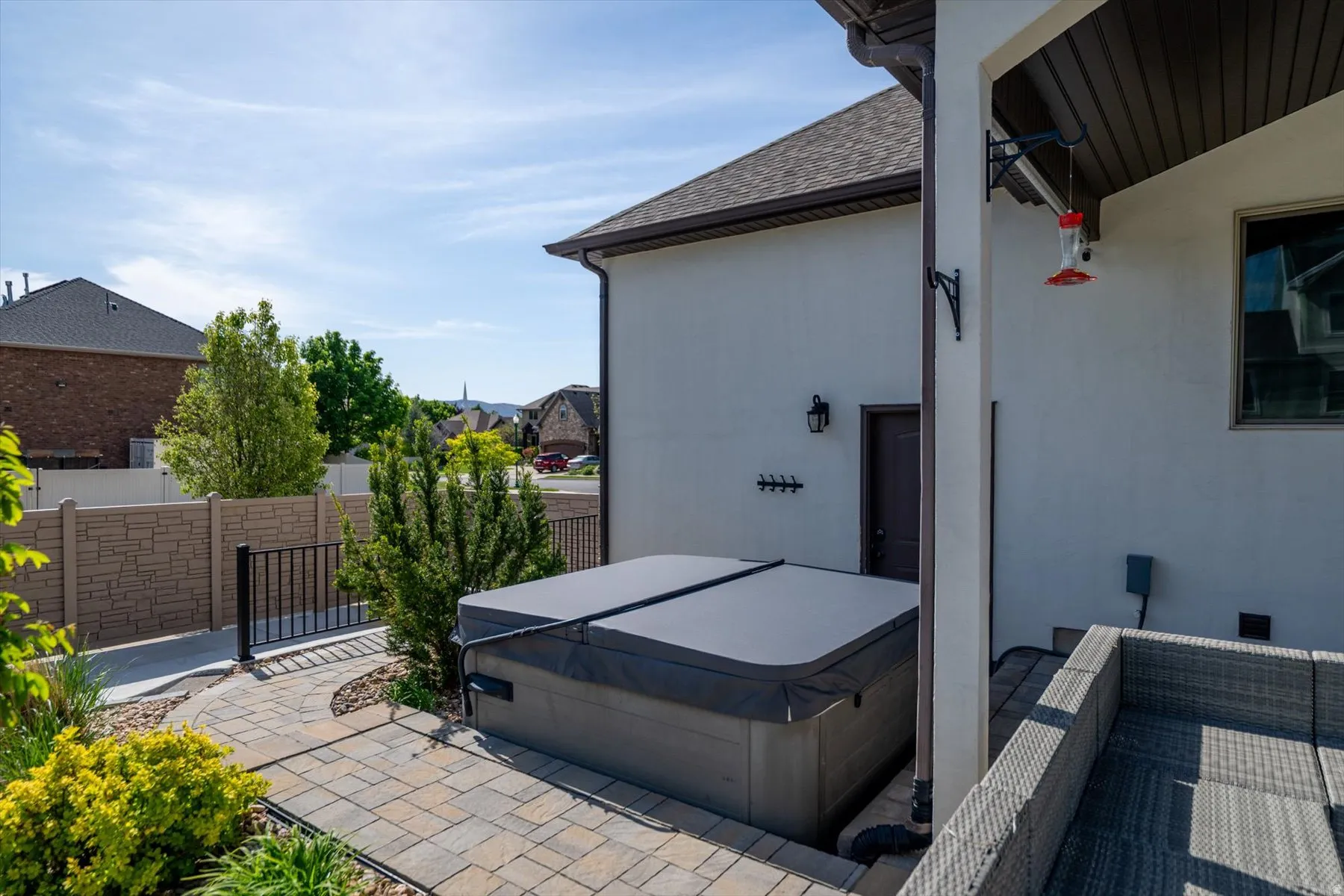 Patio area featuring a built-in hot tub with cover, paver stone walkway, stucco exterior, and a privacy fence with a metal gate