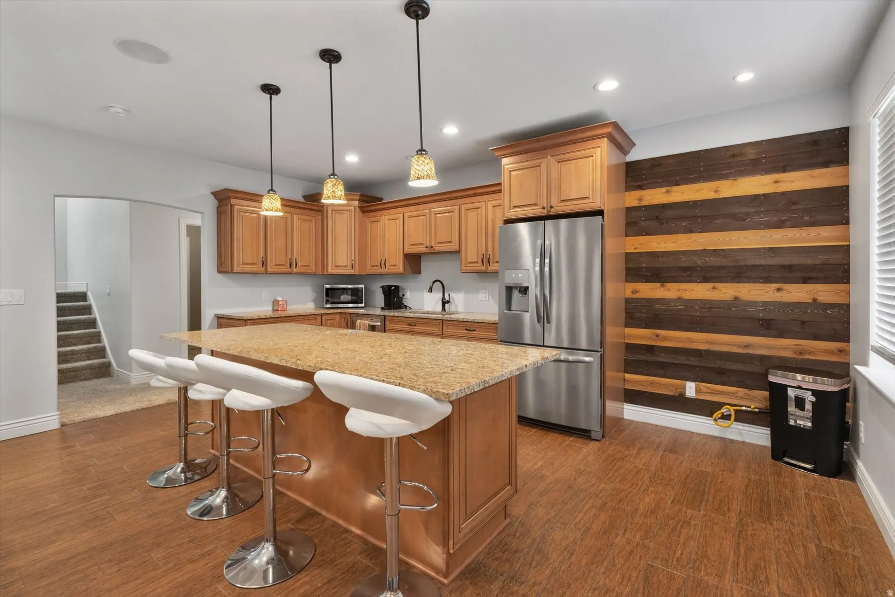 Basement kitchen featuring wood-finish flooring, light wood cabinetry, stainless steel refrigerator, and pendant lighting
