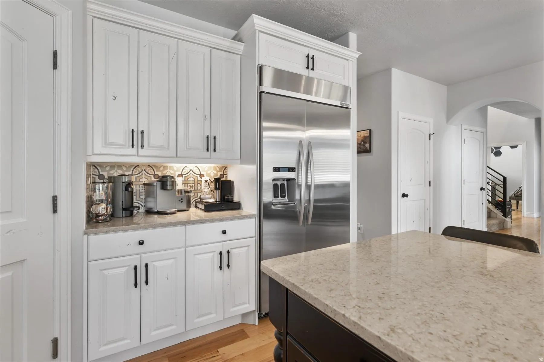 Kitchen featuring white cabinetry, stainless steel refrigerator, patterned backsplash, light-toned countertop, and dark island base