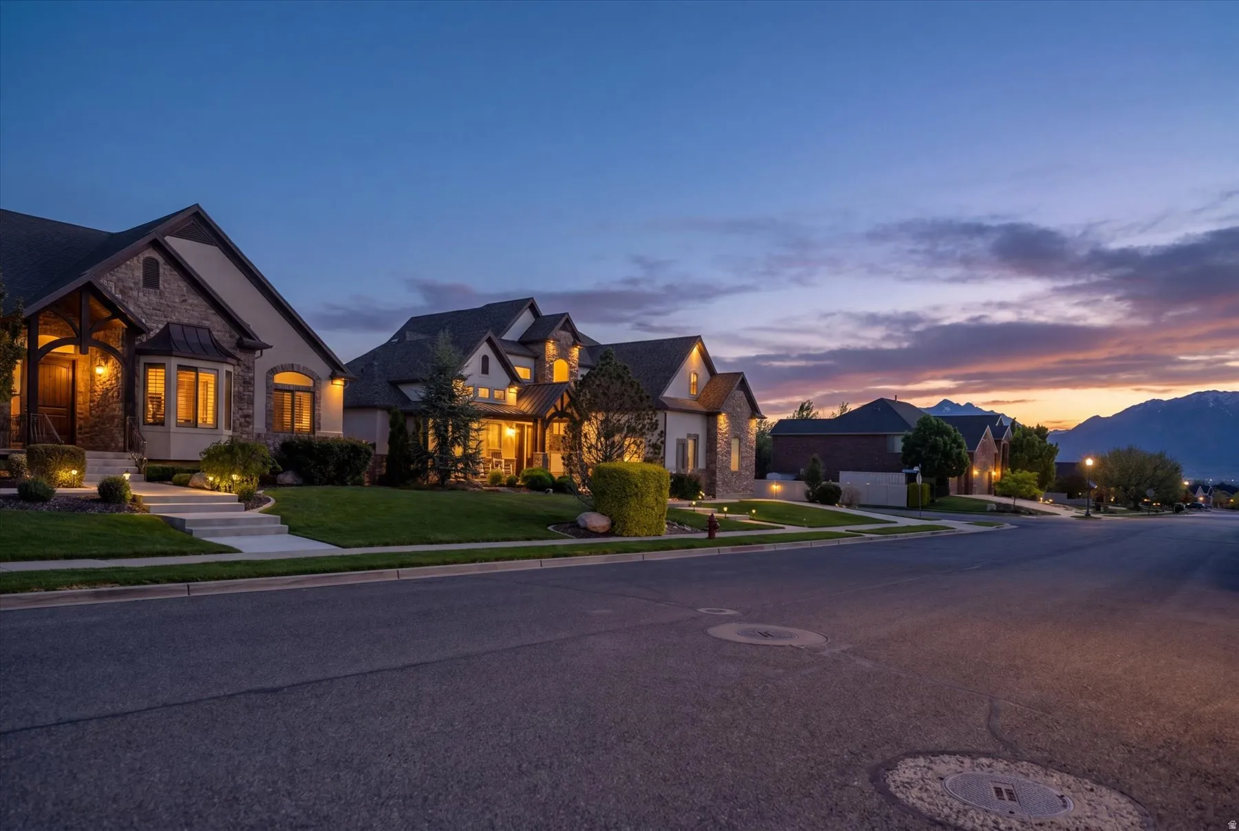 Stone and stucco exterior with architectural roofline, illuminated landscaping, bay window, and covered entryway