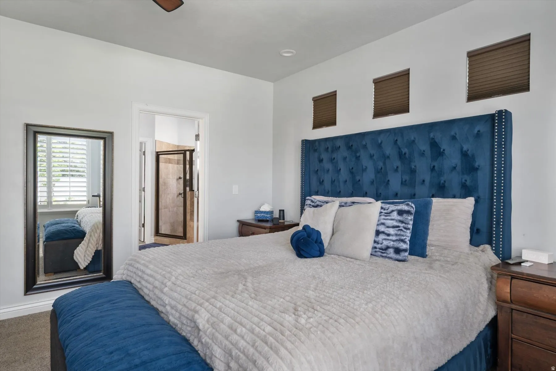Primary bedroom featuring a ceiling fan, three horizontal windows with blinds, and a doorway to a tiled shower with a glass enclosure