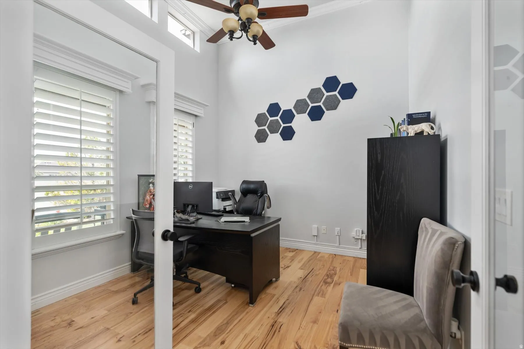 Office featuring wood-finish flooring, white plantation shutters, and a ceiling fan with integrated lighting