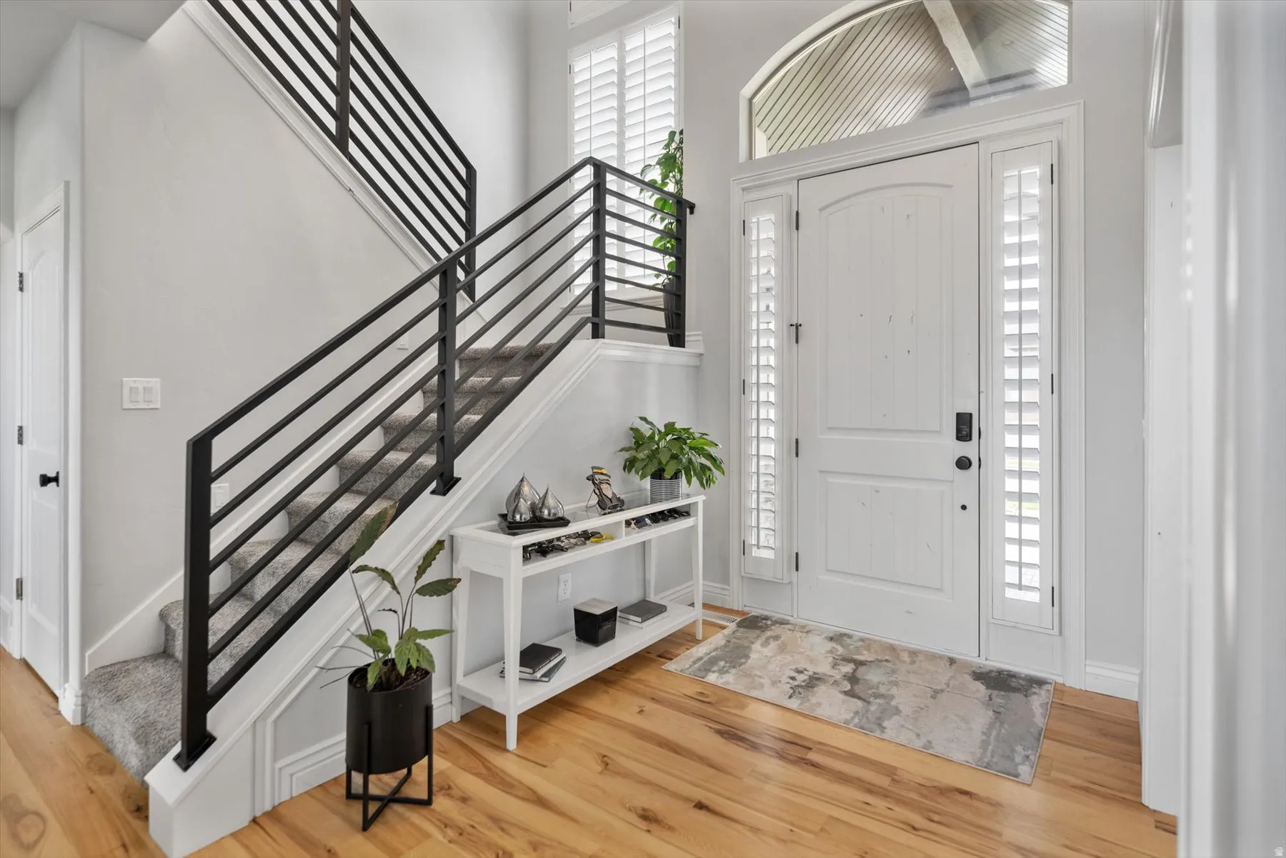 Entryway featuring a white paneled front door with matching side windows, an arched transom, and light wood-finish flooring
