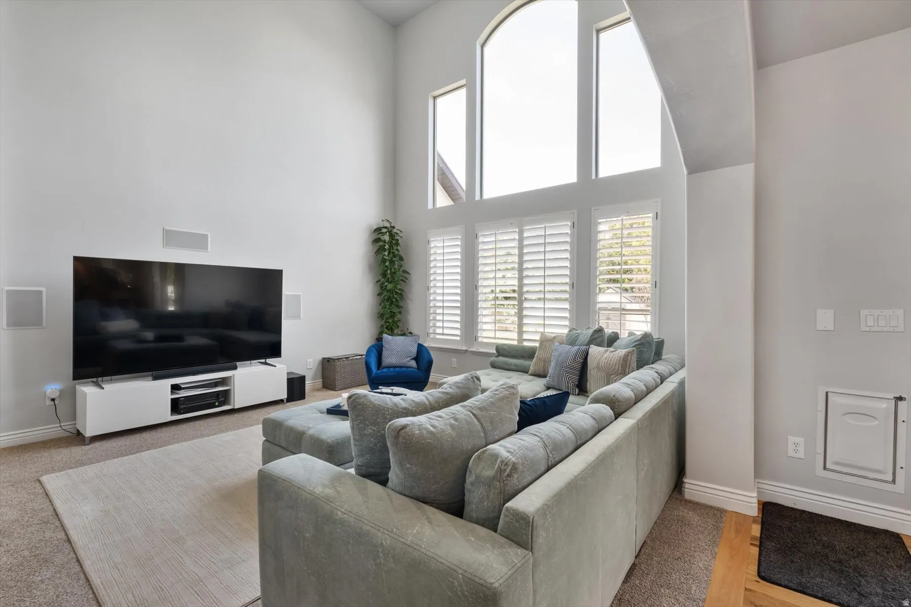 Living area featuring vaulted ceilings, a large arched window with adjacent windows, and plantation shutters