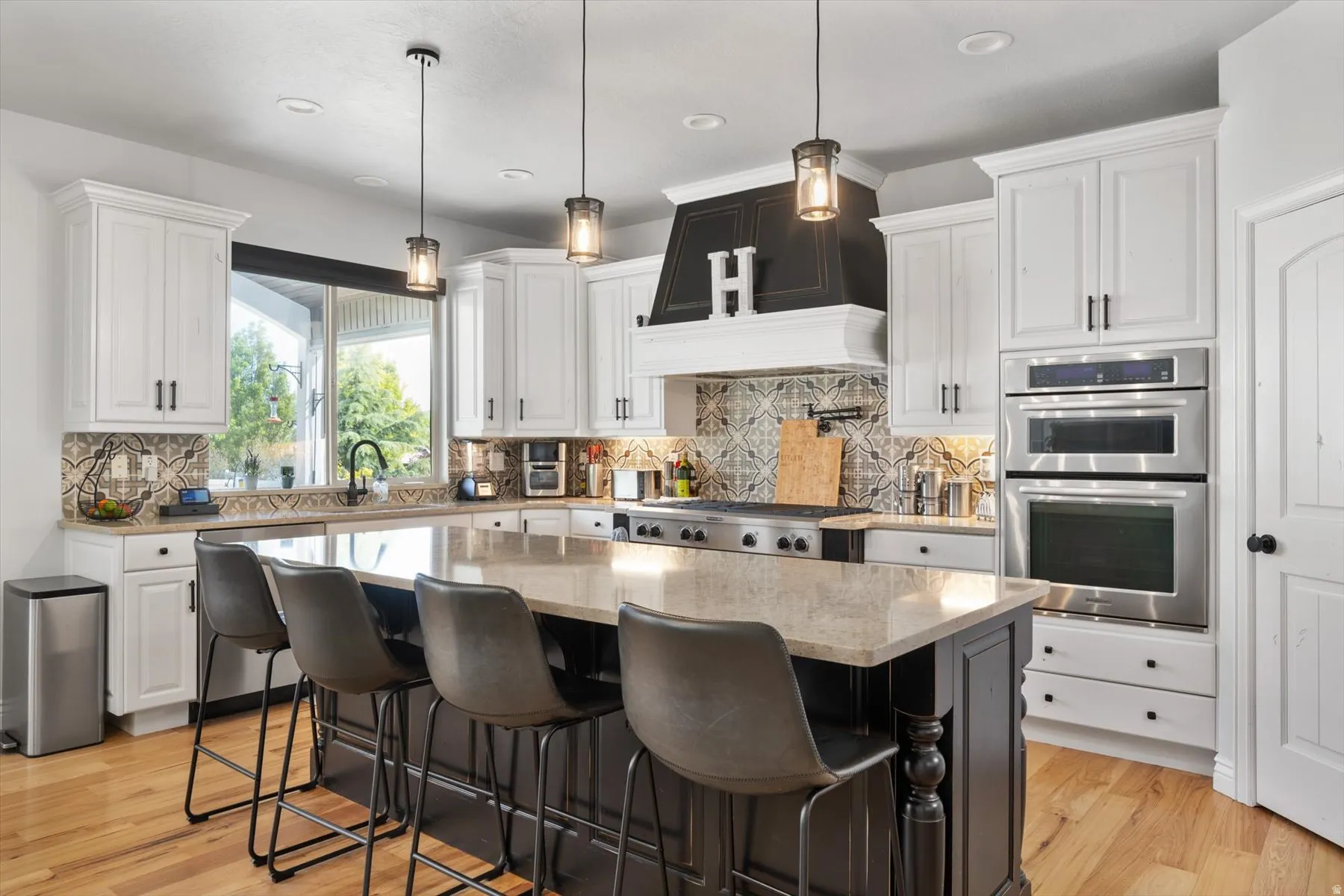Gourmet kitchen featuring a large central island with seating, stainless steel appliances including double ovens and a professional range, white cabinetry, and wood-finish flooring