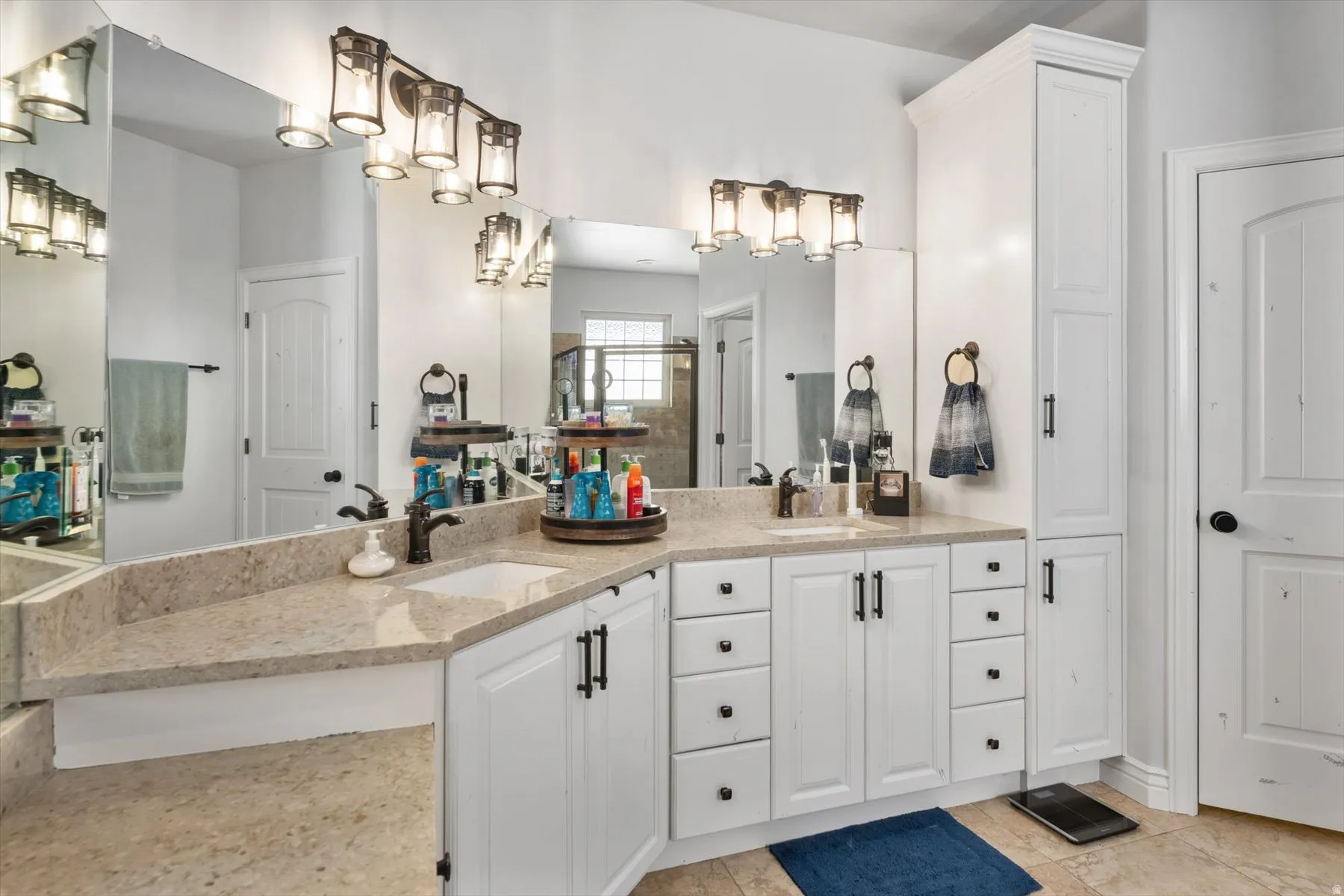 Primary bathroom ensuite with dual vanity with integrated sinks, light-toned countertops, white cabinetry, and bronzed lighting fixtures