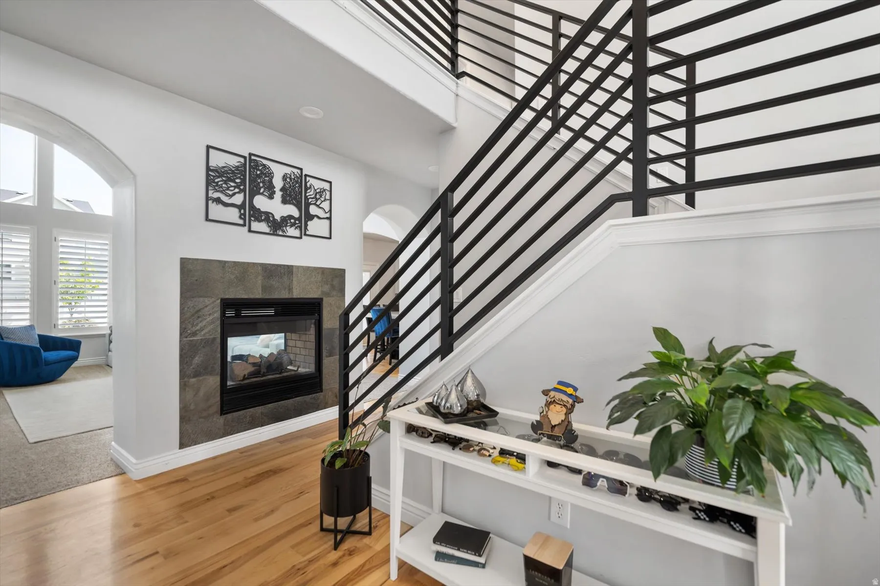 Two-story entryway featuring wood-finish flooring, a contemporary fireplace with a stone surround, and modern black horizontal stair railings