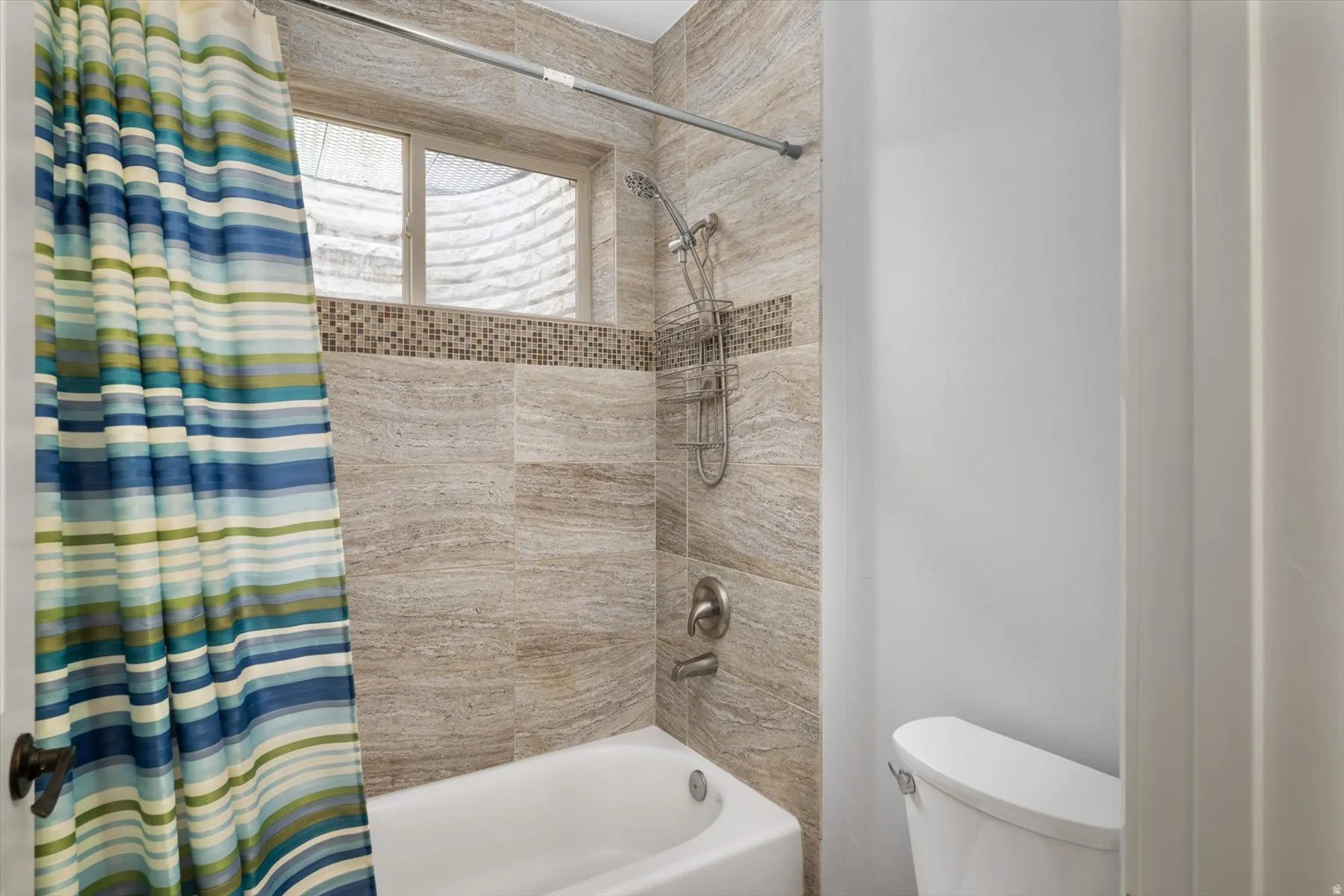 Full bathroom featuring a white bathtub, light-toned tile surround, decorative mosaic tile accent, and a single-pane window