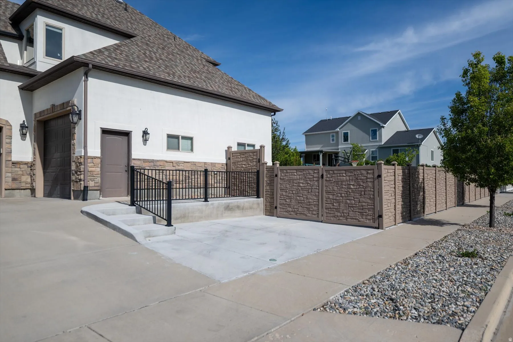 Stucco exterior with stone veneer accents, an attached garage, a concrete driveway, and a stone-patterned privacy fence