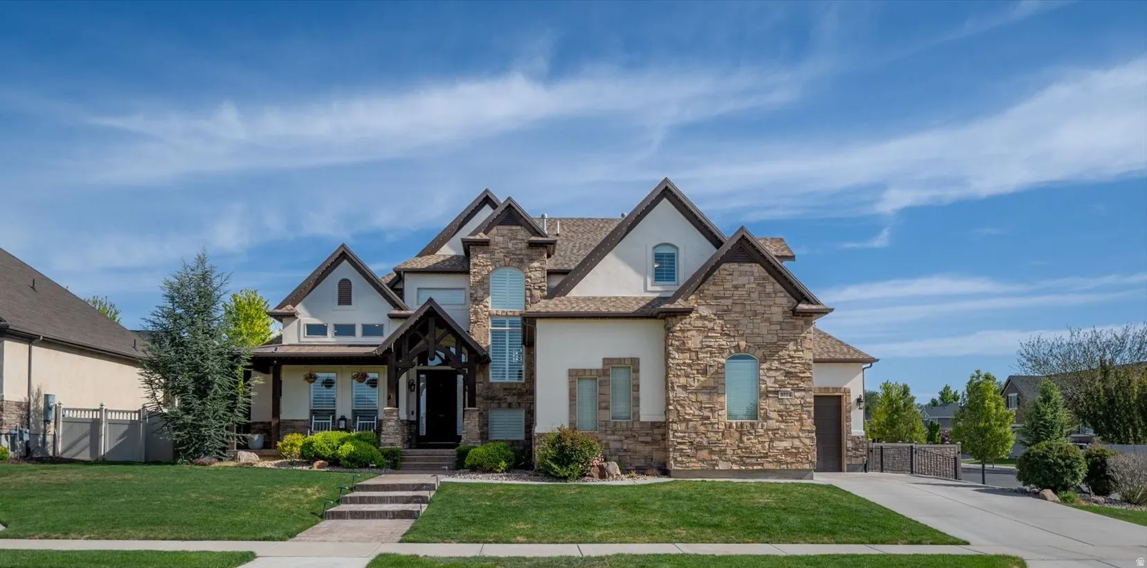Stately residence featuring stone and stucco exterior finishes, a covered front porch, and a multi-gabled roofline