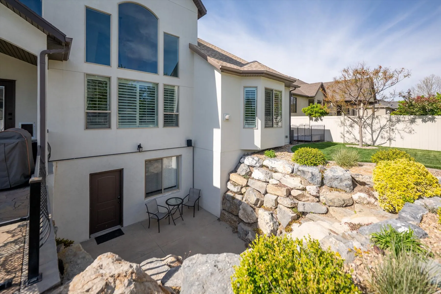 Rear exterior featuring a lower-level patio with private entry, a stone retaining wall, and a sloped lawn area
