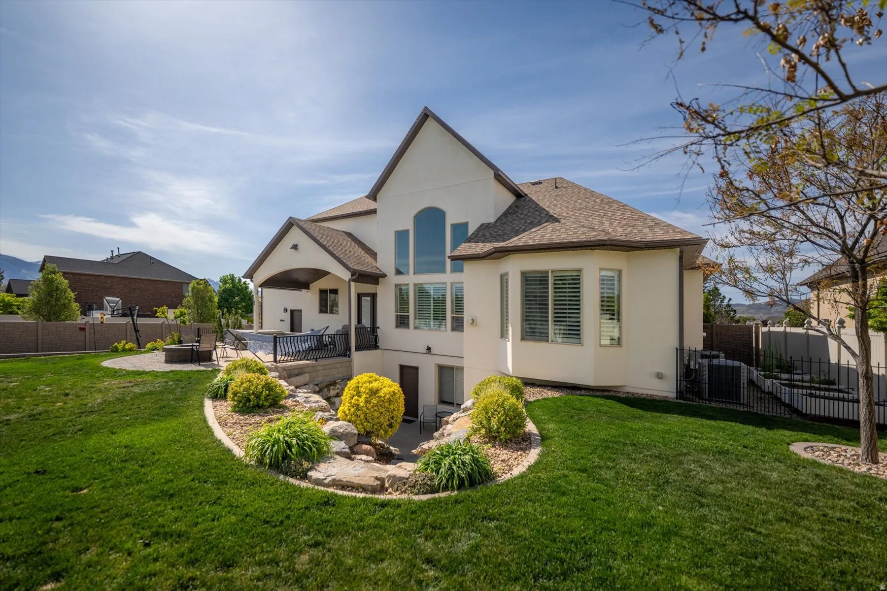 Expansive backyard featuring a manicured lawn, tiered landscaping with established plantings, and a stone-paved patio area