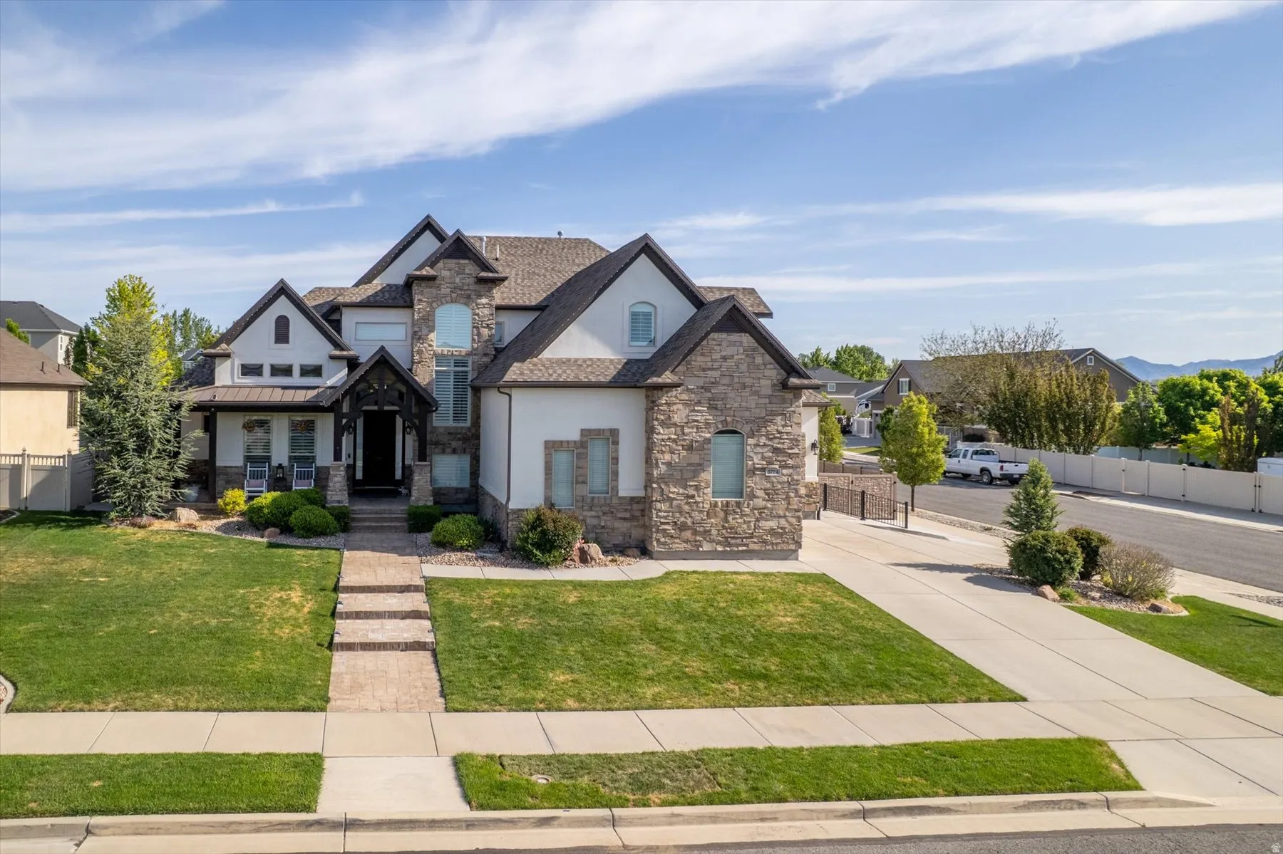 Stately residence featuring a stone and stucco exterior, dark trim accents, a prominent covered entry, a concrete driveway, and a stone-paver walkway