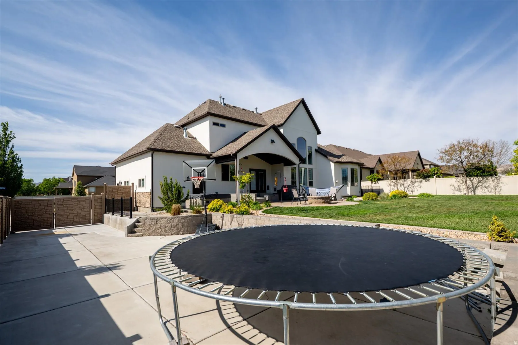 Spacious rear yard with a concrete patio, landscaped retaining walls, and a manicured lawn
