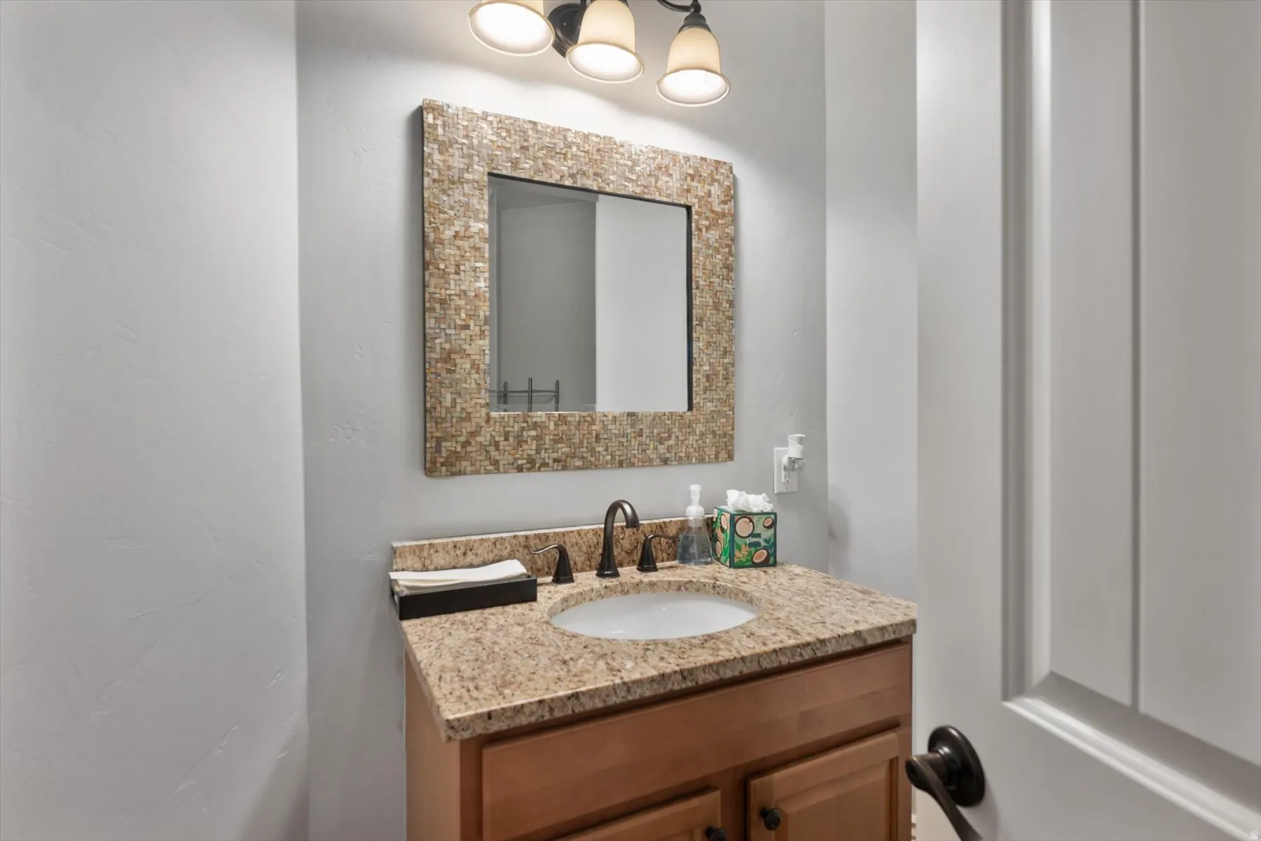 Half bathroom vanity featuring a speckled countertop, undermount sink, and a dark bronze faucet