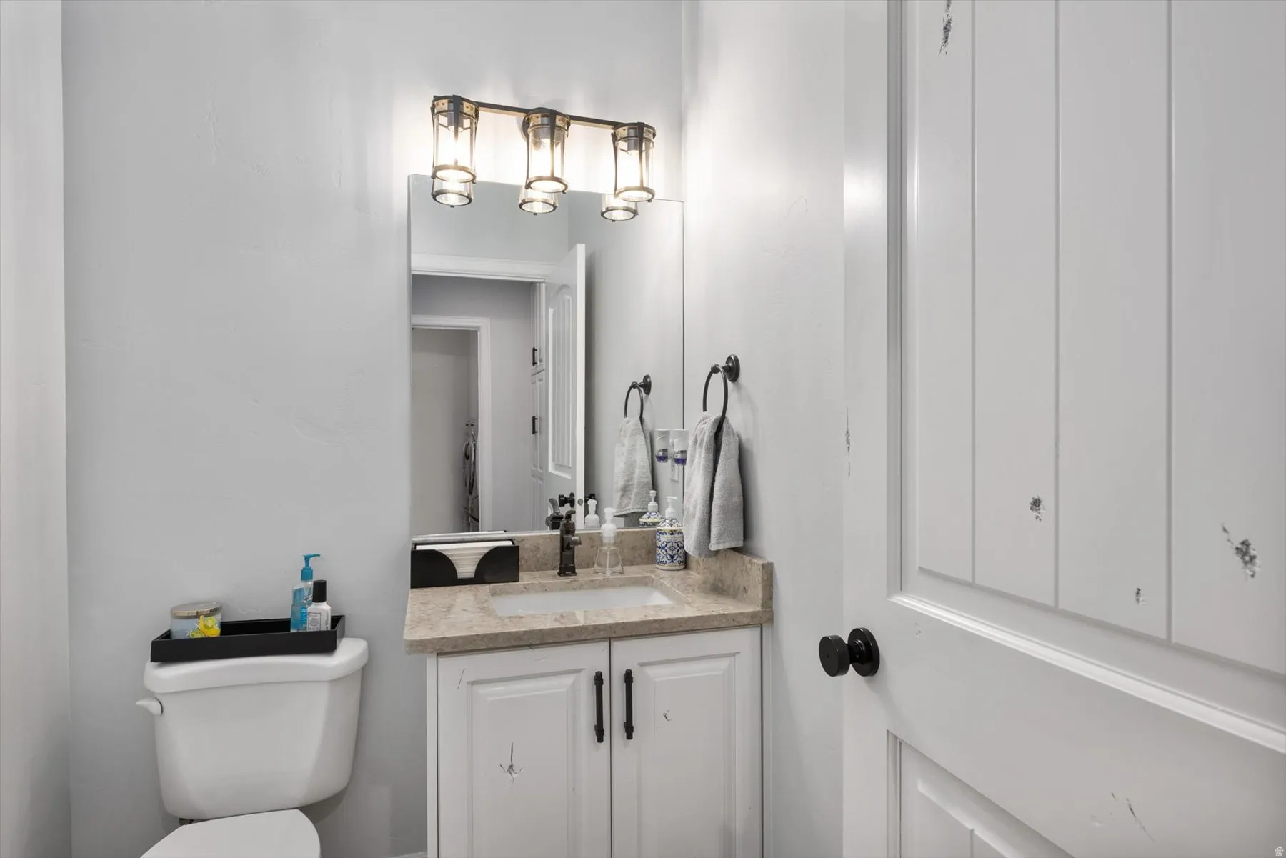 Half bathroom vanity featuring a light-toned countertop, white cabinetry with dark hardware, and a framed mirror
