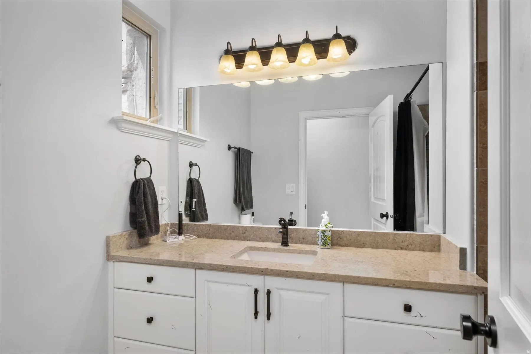 Full bathroom vanity featuring a light-toned countertop, white cabinetry with dark hardware, an undermount sink, and a dark-finish faucet