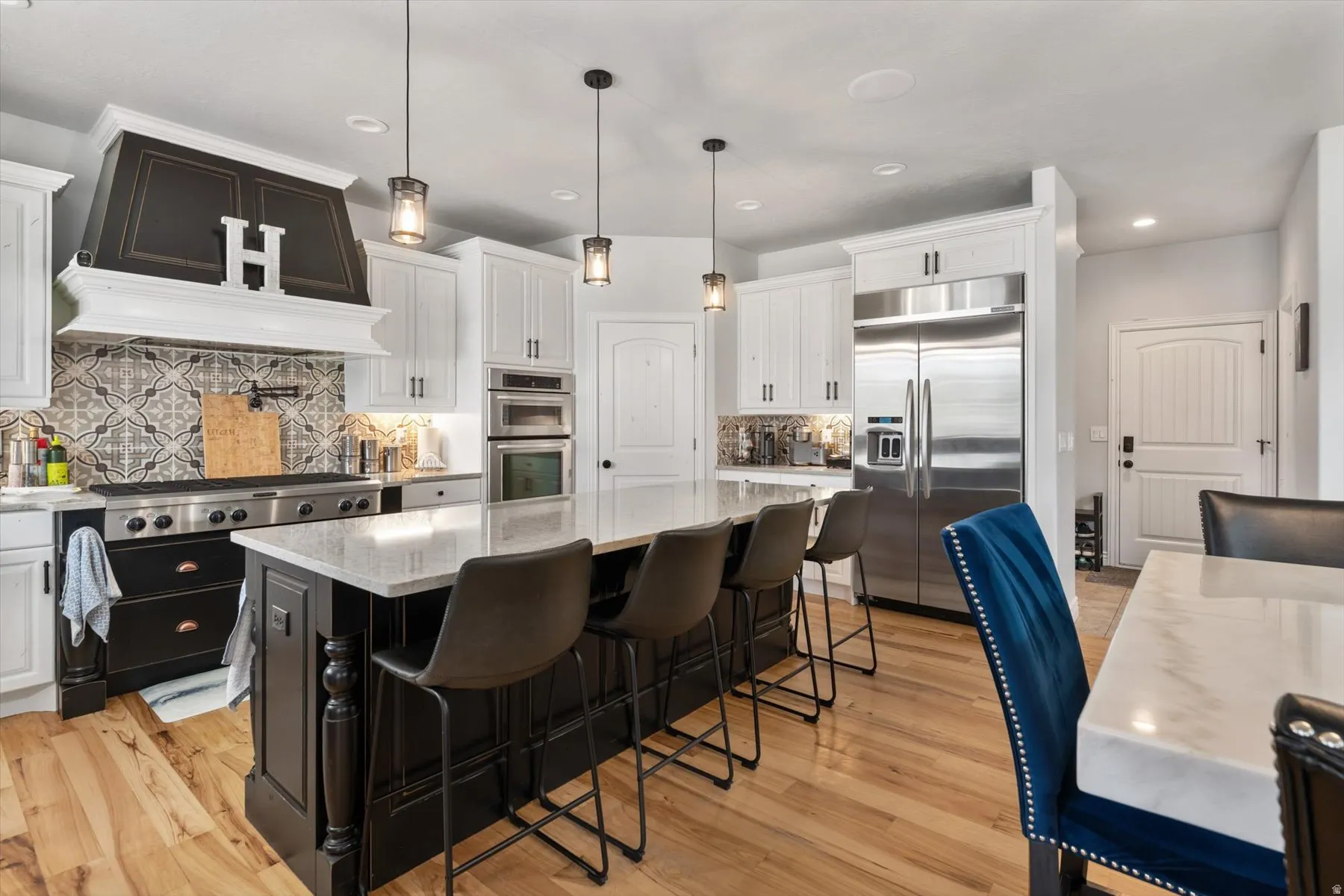 Gourmet kitchen featuring a substantial central island, stainless steel appliances, a custom range hood, patterned tile backsplash, and light wood-finish flooring