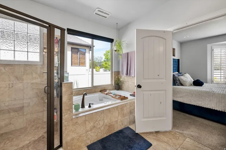 Primary bathroom ensuite with soaking jetted tub with bronze faucet, glass-enclosed shower with bronze frame, large window, & tile flooring