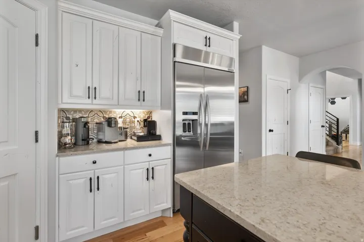 Kitchen featuring white cabinetry, stainless steel refrigerator, patterned backsplash, light-toned countertop, and dark island base