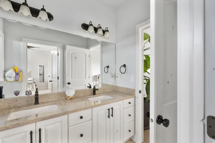 Full bathroom vanity featuring dual undermount sinks, a light-toned countertop, and white cabinetry with dark hardware