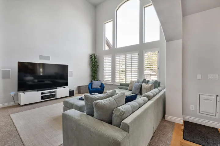 Living area featuring vaulted ceilings, a large arched window with adjacent windows, and plantation shutters