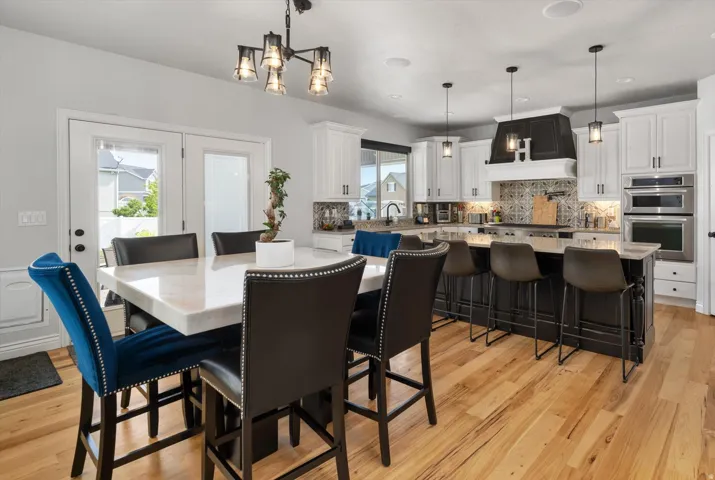 Open-concept kitchen and dining area featuring light-toned wood flooring, white cabinetry, and a dark-toned kitchen island with bar seating
