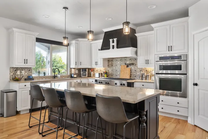 Gourmet kitchen featuring a large central island with seating, stainless steel appliances including double ovens and a professional range, white cabinetry, and wood-finish flooring