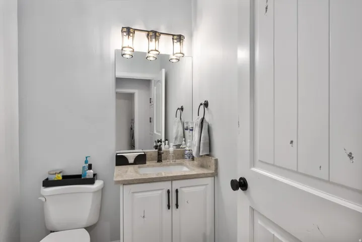 Half bathroom vanity featuring a light-toned countertop, white cabinetry with dark hardware, and a framed mirror