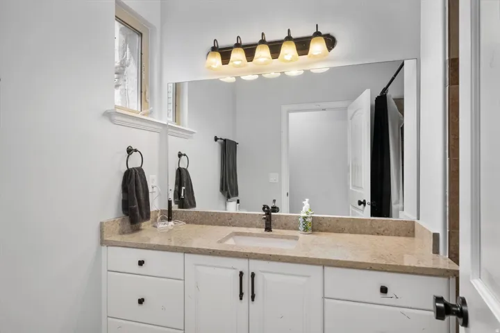 Full bathroom vanity featuring a light-toned countertop, white cabinetry with dark hardware, an undermount sink, and a dark-finish faucet