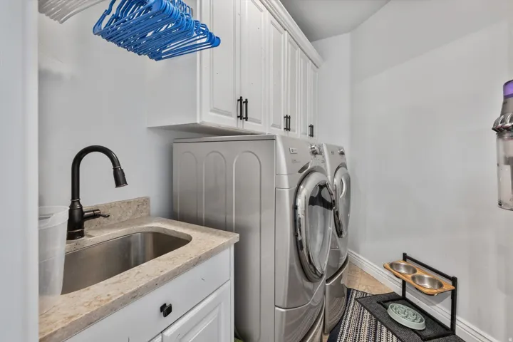 Laundry area featuring a utility sink, a dark bronze gooseneck faucet, light-toned stone-finish countertop, white cabinetry with dark hardware, and tile flooring