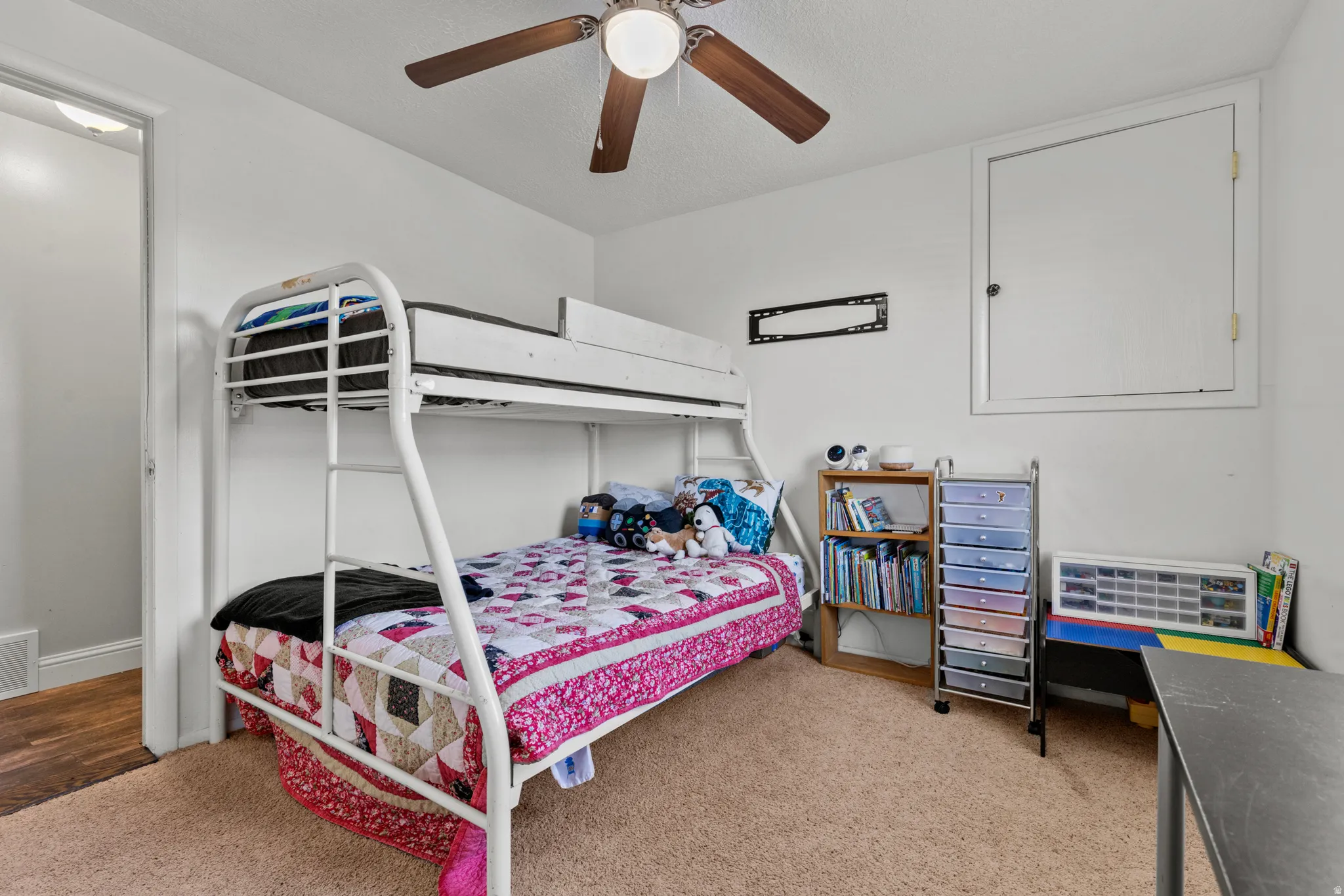 Carpeted room featuring a ceiling fan, white walls, and a recessed doorway with wood-finish flooring visible beyond