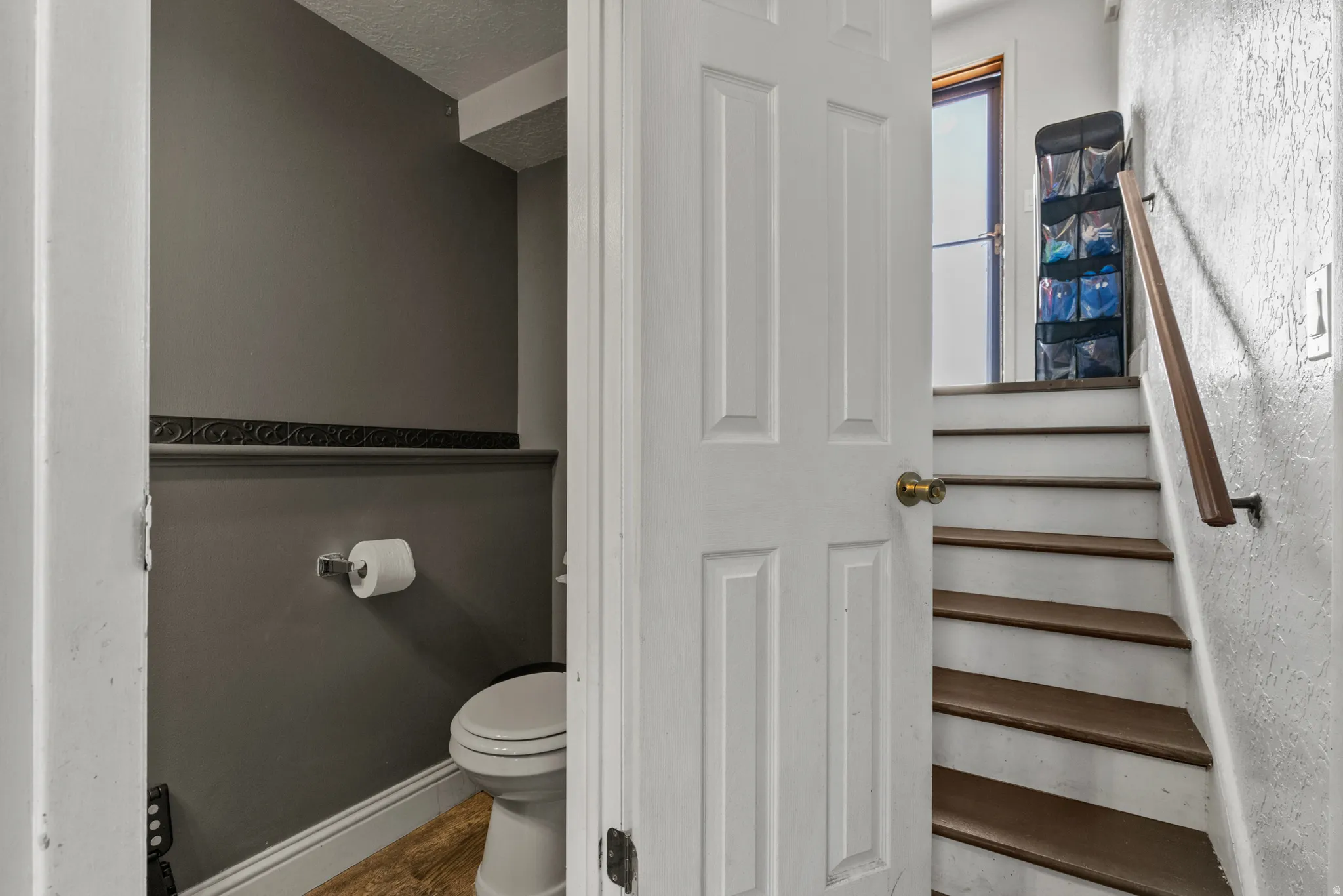 Staircase featuring wood-finish treads, painted risers, and a wall-mounted handrail