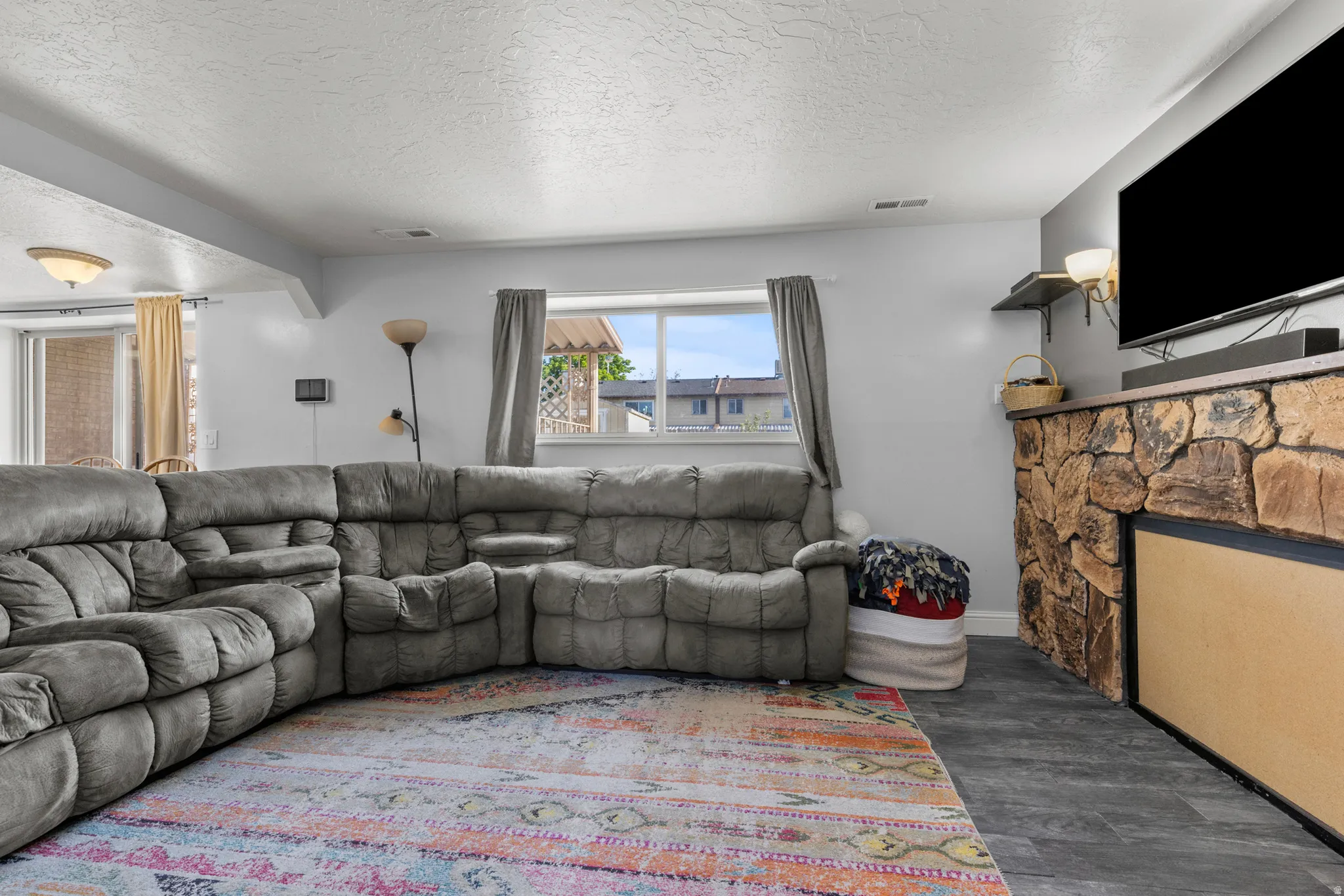Spacious room featuring durable wood-finish flooring, a stone-faced fireplace with a dark wood mantel, and light gray walls
