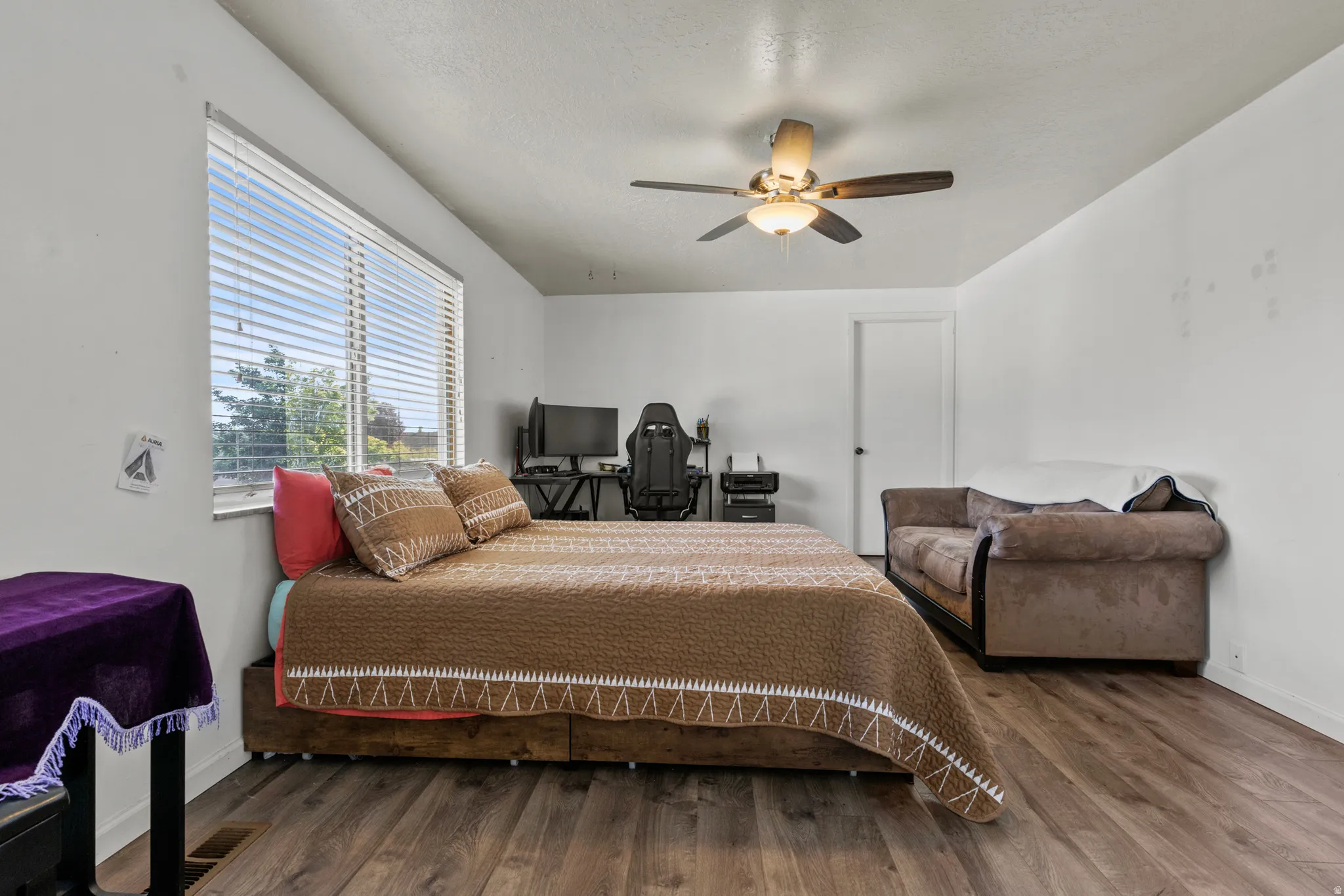 Spacious room featuring wood-finish flooring, a large window with blinds, and a ceiling fan with integrated lighting