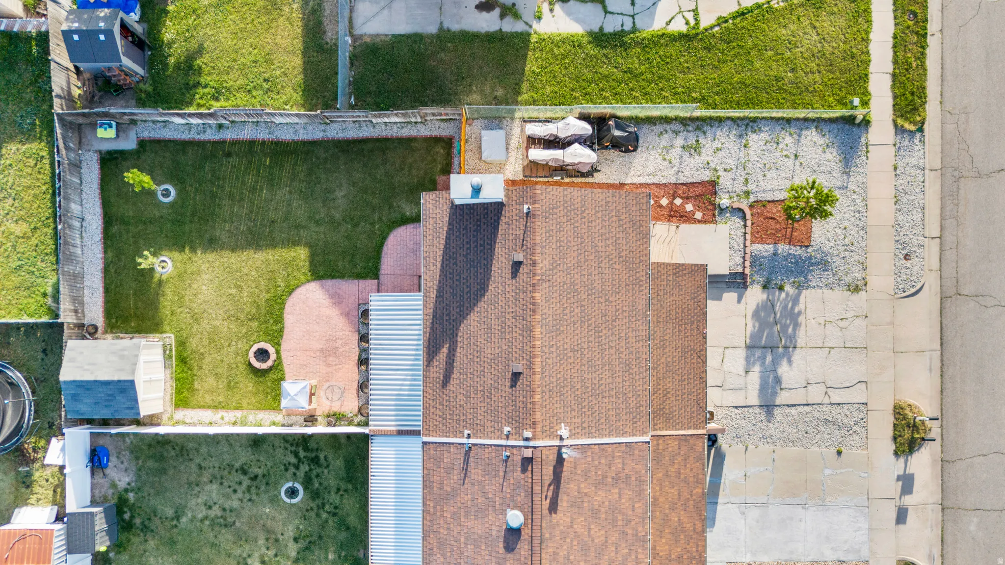 Property featuring a brown shingle roof, a backyard with a manicured lawn, a fire pit, and an attached paved patio