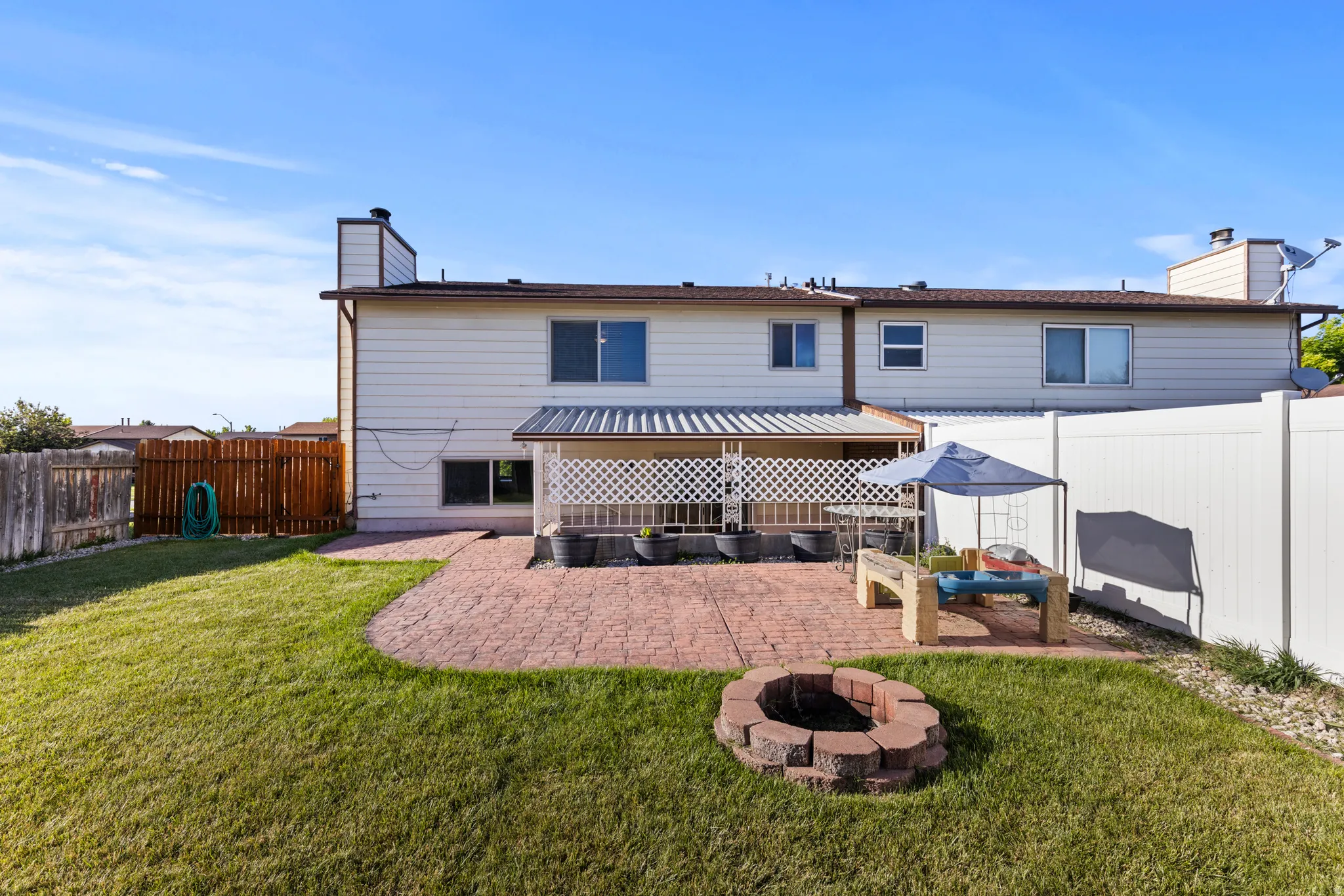 Expansive backyard featuring a patterned paver patio, a built-in fire pit, a covered porch, and a combination of wood and vinyl fencing