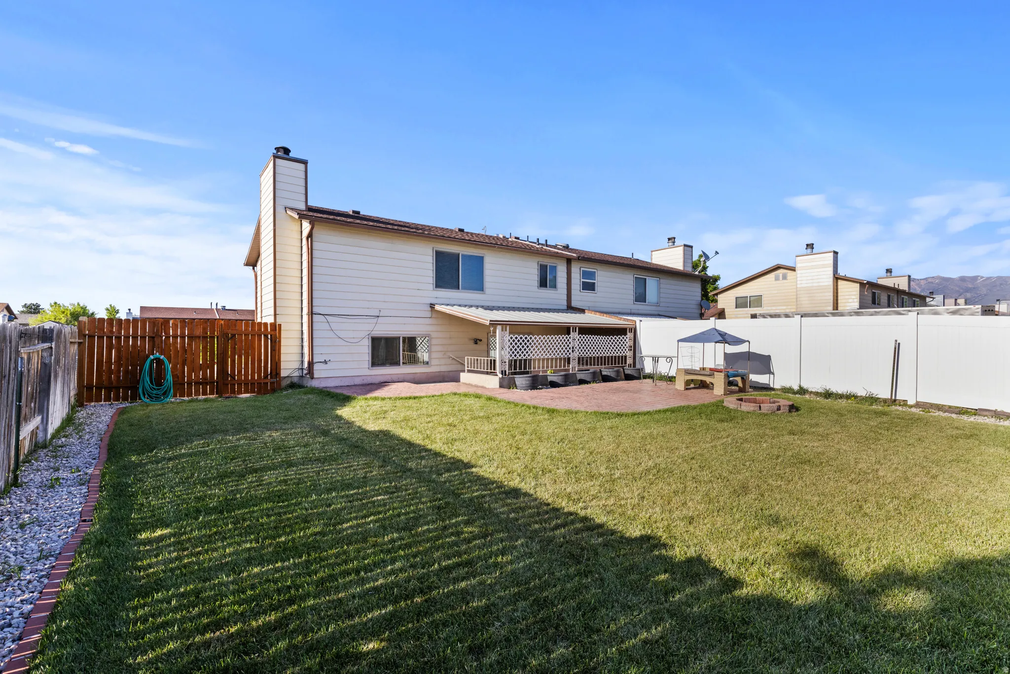 Expansive backyard featuring a covered patio, brick paver hardscaping, mature lawn, and wood privacy fencing